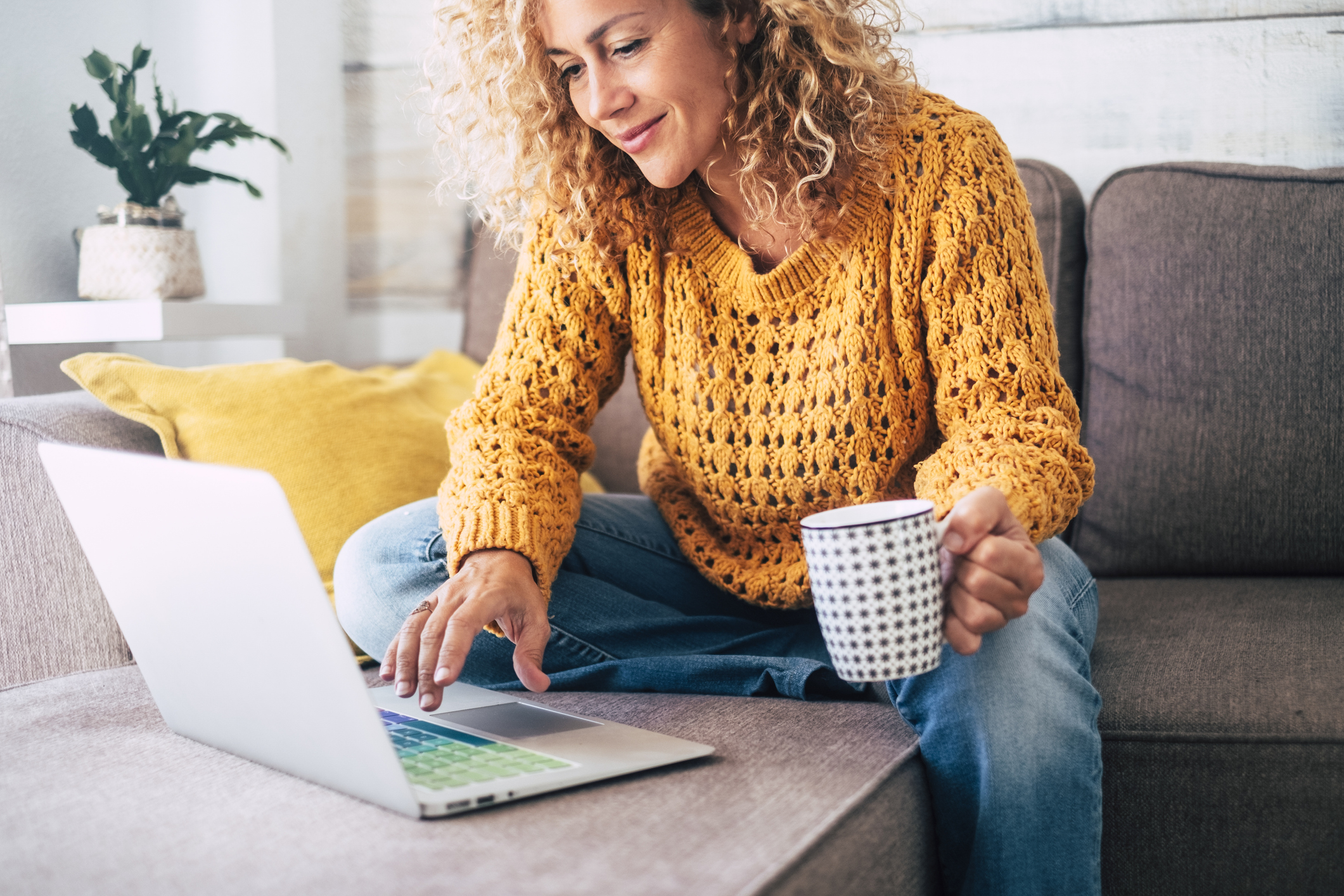 Nice beautiful lady with blonde curly hair work at the notebook sit down on the sofa at home – check on line shops for cyber monday sales – technology woman concept for alternative office freelance